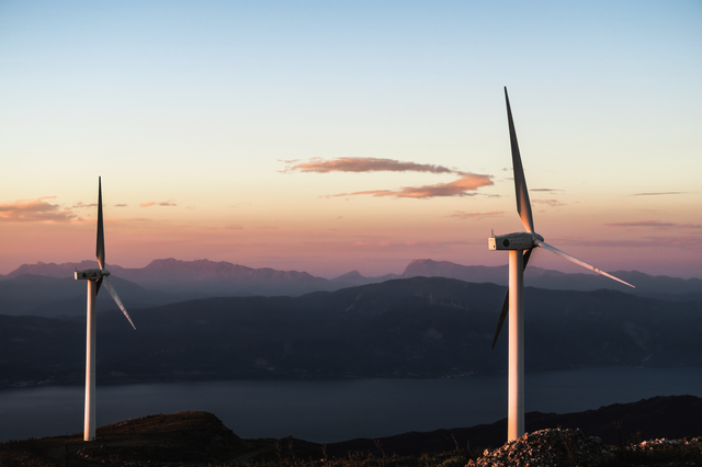 Two wind turbines with mountains and lake in the background